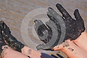 Woman hands and feet covered with black healing mud, sandy seashore in background