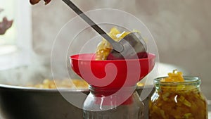 woman hands filling glass jars with apple jam via red funnel and soup ladle, slow motion closeup