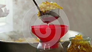 woman hands filling glass jars with apple jam via red funnel and soup ladle, slow motion closeup