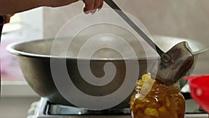 woman hands filling glass jars with apple jam via red funnel and soup ladle, slow motion closeup