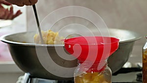 woman hands filling glass jars with apple jam via red funnel and soup ladle, slow motion closeup