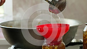 woman hands filling glass jars with apple jam via red funnel and soup ladle, slow motion closeup