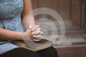 Woman hands folded in prayer on a Holy Bible for faith concept