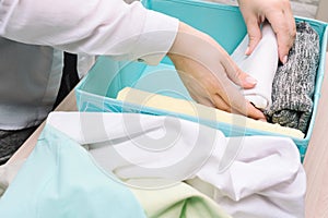 Woman hands folds her clothes and puts them in blue storage box. Vertical storage of clothing, tidying up, room cleaning