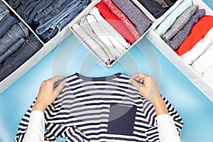 Woman hands folds and puts clothes to baskets. Vertical clothing storage, tidying up, declutter, room cleaning. Top view