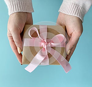 Woman hands give handmade present wrapped in craft paper with soft pink ribbon