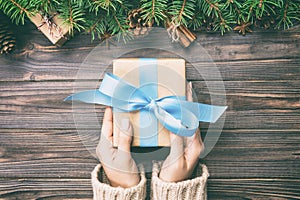Woman hands give wrapped christmas handmade present in paper with blue ribbon. Present box on holiday on dark wooden table, top