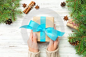 Woman hands give wrapped christmas handmade present in paper with blue ribbon. Present box on holiday on white wooden