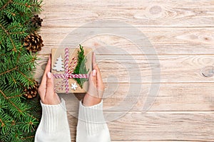 Woman hands give wrapped christmas handmade present in paper with christmas decoration. Present box on holiday on dark wooden tabl