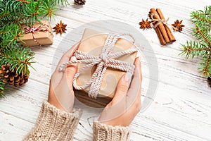 Woman hands give wrapped christmas handmade present in paper with pink ribbon. Present box on holiday on white wooden