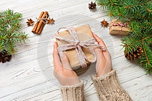 Woman hands give wrapped christmas handmade present in paper with pink ribbon. Present box on holiday on white wooden table, top v