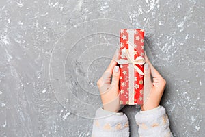 Woman hands give wrapped christmas or other holiday handmade present in colored paper . Present box, decoration of gift on gray