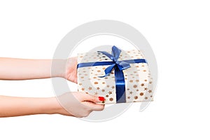 Woman hands give wrapped Christmas or other holiday handmade present in gold paper with blue ribbon. Isolated on white background