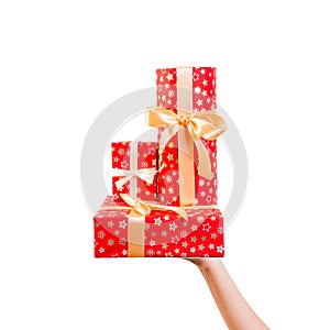 Woman hands give wrapped group of Christmas or other holiday handmade present in red paper with Gold ribbon. Isolated on white