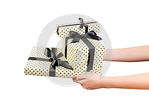 Woman hands give wrapped group of Christmas or other holiday handmade present in yellow paper with black ribbon. Isolated on white