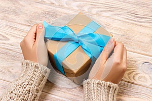 Woman hands give wrapped valentine or other holiday handmade present in paper with blue ribbon. Present box, decoration of gift on