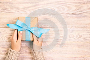 Woman hands give wrapped valentine or other holiday handmade present in paper with blue ribbon. Present box, decoration of gift on