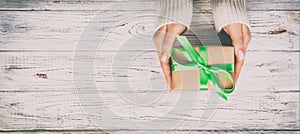 Woman hands give wrapped valentine or other holiday handmade present in paper with green ribbon. Present box, decoration of gift