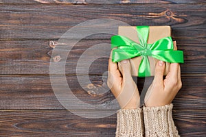 Woman hands give wrapped valentine or other holiday handmade present in paper with green ribbon. Present box, decoration of gift o