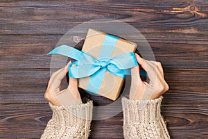 Woman hands give wrapped valentine or other holiday handmade present in paper with blue ribbon. Present box, decoration of gift on