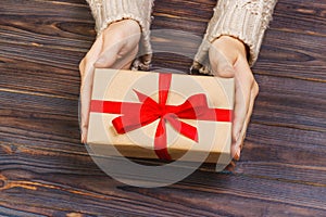 Woman hands give wrapped valentine or other holiday handmade present in paper with red ribbon. Present box, decoration of gift on