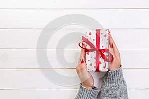Woman hands give wrapped valentine or other holiday handmade present in paper with red ribbon. Present box, red heart decoration