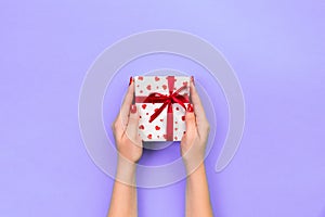 Woman hands give wrapped valentine or other holiday handmade present in paper with red ribbon. Present box, red heart decoration