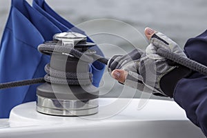 Woman hands in gloves holding the rope on sailing boat yacht sheet winch closeup on water sea background