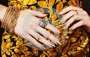 Woman hands with golden manicure lot of jewelry on fancy dress close up beauty concept