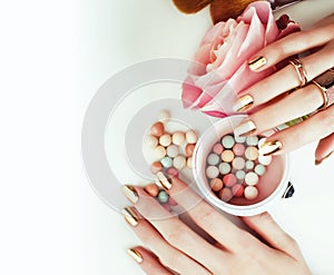 woman hands with golden manicure and many rings holding brushes, cosmetic and rose flower on white background, spa