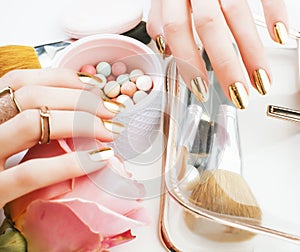 woman hands with golden manicure and many rings holding brushes, cosmetic and rose flower on white background, spa