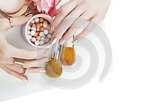 woman hands with golden manicure and many rings holding brushes, cosmetic and rose flower on white background, spa