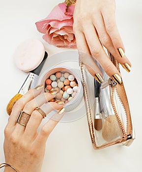 woman hands with golden manicure and many rings holding brushes, cosmetic and rose flower on white background, spa