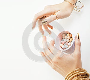 woman hands with golden manicure and many rings holding brushes, cosmetic and rose flower on white background, spa