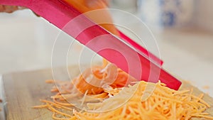 Woman hands grates carrots on red grate at kitchen table