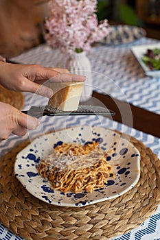 Woman hands grating parmesan cheese to homemade spaghetti bolognese