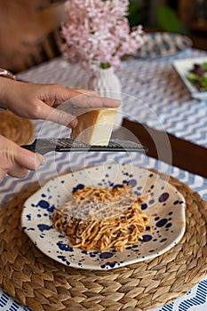 Woman hands grating parmesan cheese to homemade spaghetti bolognese