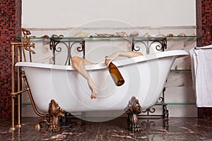 Woman hands hanging from the bathtube, with epmty wine bottle.