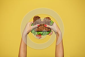 Woman hands hold bitten sandwich on yellow background. Sandwich promotion concept