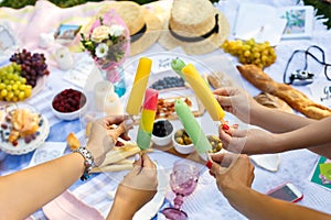 Woman hands hold colorful ice-cream sticks at summer picnic background. Summer weekends