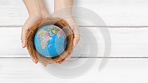 Woman hands hold the globe on bird nest over white wood background with copy space. protect and save our world from  disease