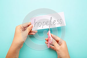 Woman hands hold a paper with the word Hopeless, cut it with scissors to make Hope