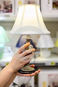 Woman hands hold table lamp in shop