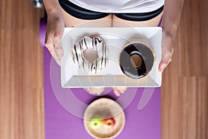 Woman hands holding baked donut during standing on yoga mat ,Healthy diet,Dieting concept,Top view