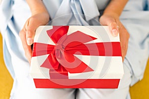 Woman hands holding beautiful giftbox with red bow. Festive red and white present box in woman's hands