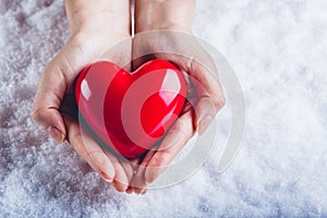 Woman hands are holding a beautiful glossy red heart in a snow background. Love and St. Valentine concept.