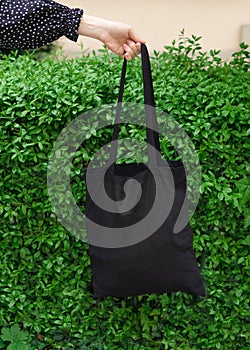 Woman hands holding black bag canvas fabric for mockup blank template isolated on green grass background.