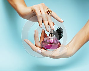 Woman hands holding bottle of perfume pink manicure and jewelry on blue background, luxury concept