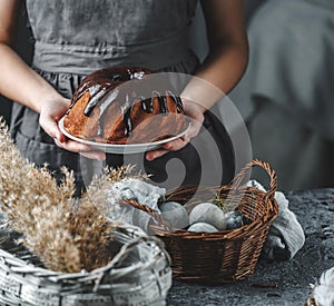 Woman hands holding chocolate Easter cake on table decorated with spring flowers and nest with eggs. Happy Easter holiday,