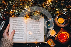 Woman hands holding Christmas Book. reading fairytale Story in cozy home evening. Christmas Holiday mood. New Eve candle lights on